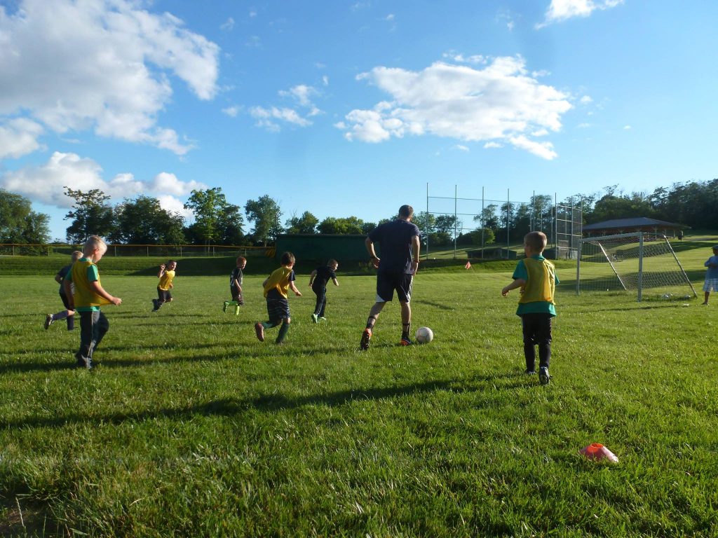 coach dribbling soccer ball with kids running alongside